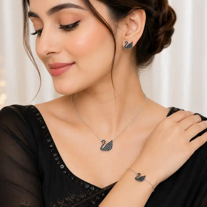 A woman wearing a matching jewelry set featuring a silver-toned necklace, bracelet, and stud earring with a swan motif set with dark blue stones, wearing a black embroidered blouse.