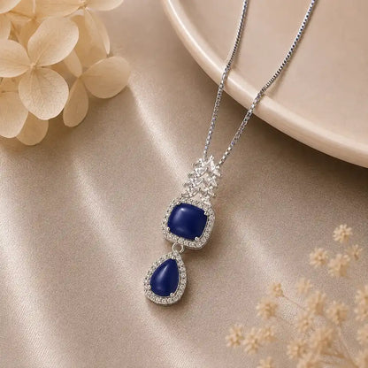 Silver Celestial Drop Pendant Necklace featuring a square and teardrop double-halo pendant set with deep blue stones and sparkling clear zircon crystal accents.