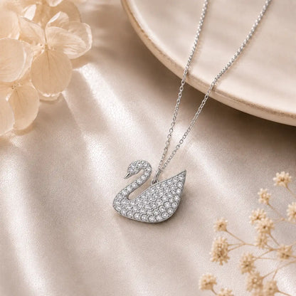 Silver-tone Elegant Swan Crystal Pendant Necklace fully pavé-set with shimmering white crystals, displayed on a soft champagne satin background.