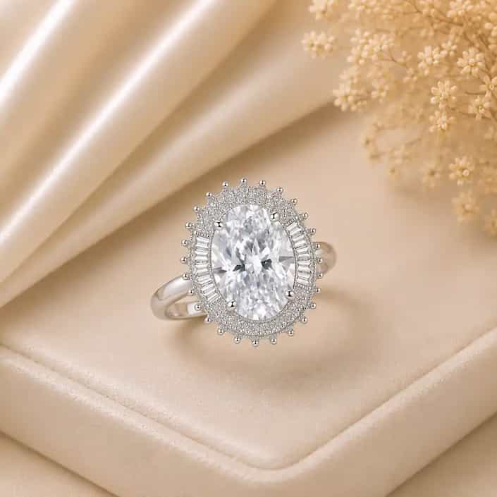 Elegant silver ring featuring a large oval black gemstone surrounded by a sparkling halo of clear stones, displayed on a cream satin jewelry box with delicate white flowers in the background.
